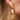 Close-up picture of Celeste: champagne colored gold long statement earrings worn on a model. Close-up foto van Celeste: champagnekleurige gouden lange oorbellen gedragen door een model.